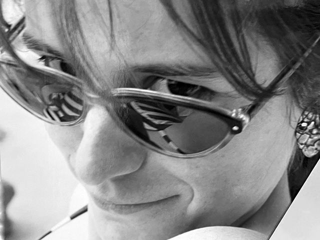 Schwarze Sonnenbrille tragende Person lächelt leicht, Porträt im Schwarz-Weiß-Stil.